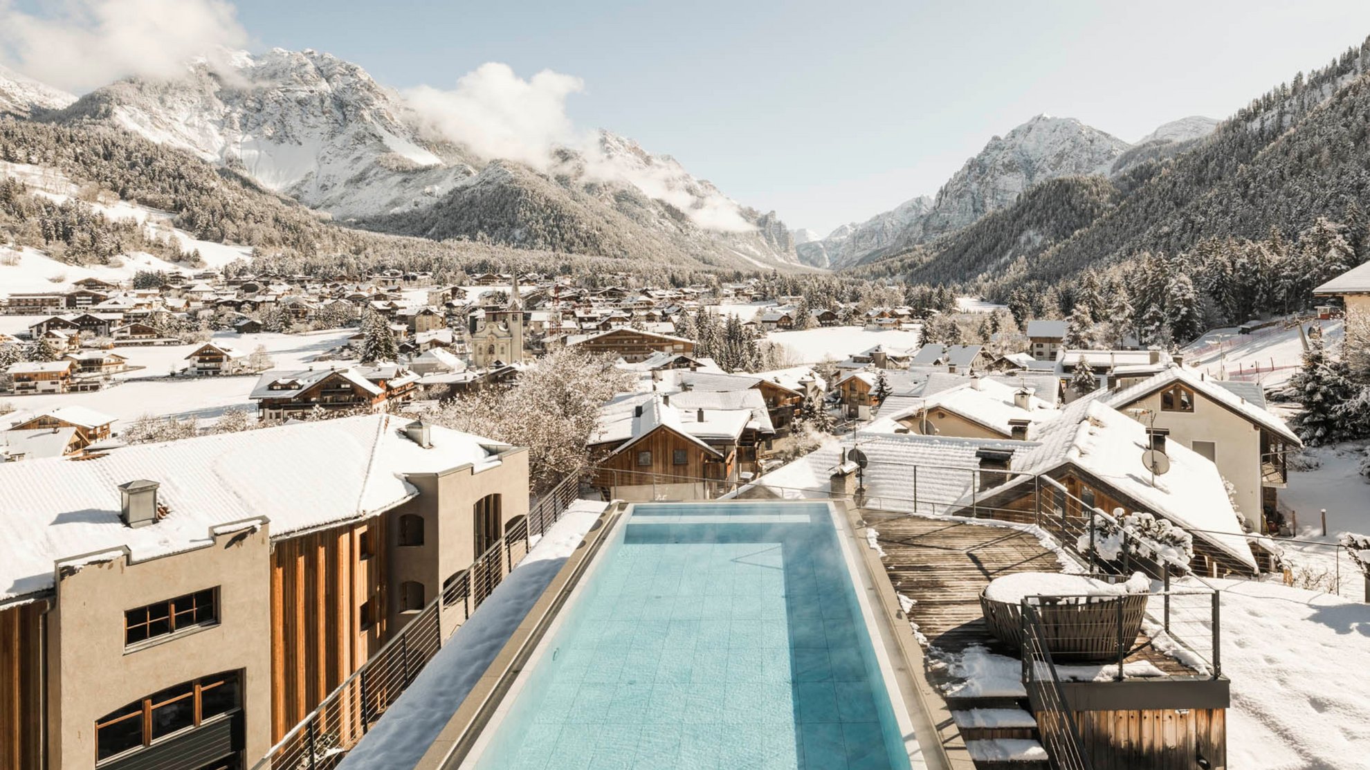 Wellnesshotel in Südtirol: Auf in den Traumurlaub! Schwimmbad auf dem Dach mit Blick auf schneebedeckte Berge und Dorf