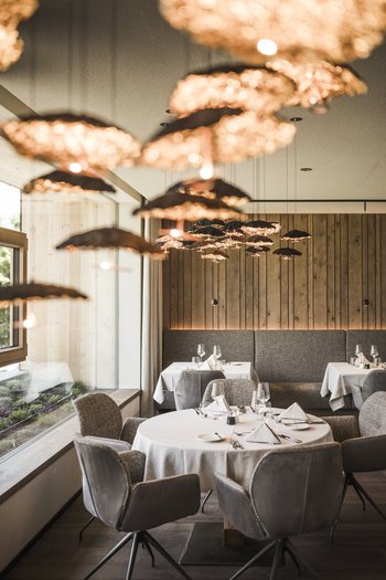 Wellnesshotel in Südtirol: Auf in den Traumurlaub! Elegantes Restaurant mit runden gedeckten Tischen und warmen Hängelichtern
