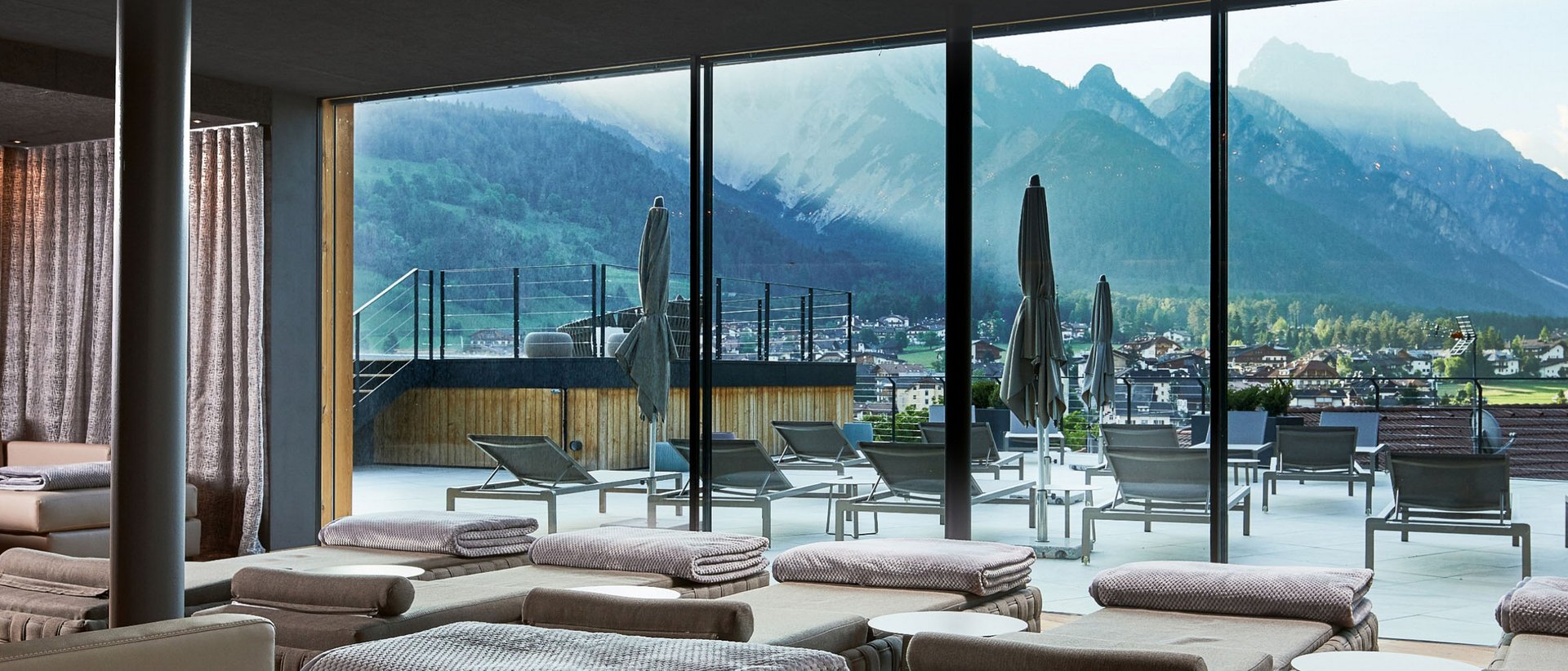 Wellnesshotel in Südtirol: Auf in den Traumurlaub! Innenraum mit Liegen und großer Glasfront, Blick auf Terrasse und Berge