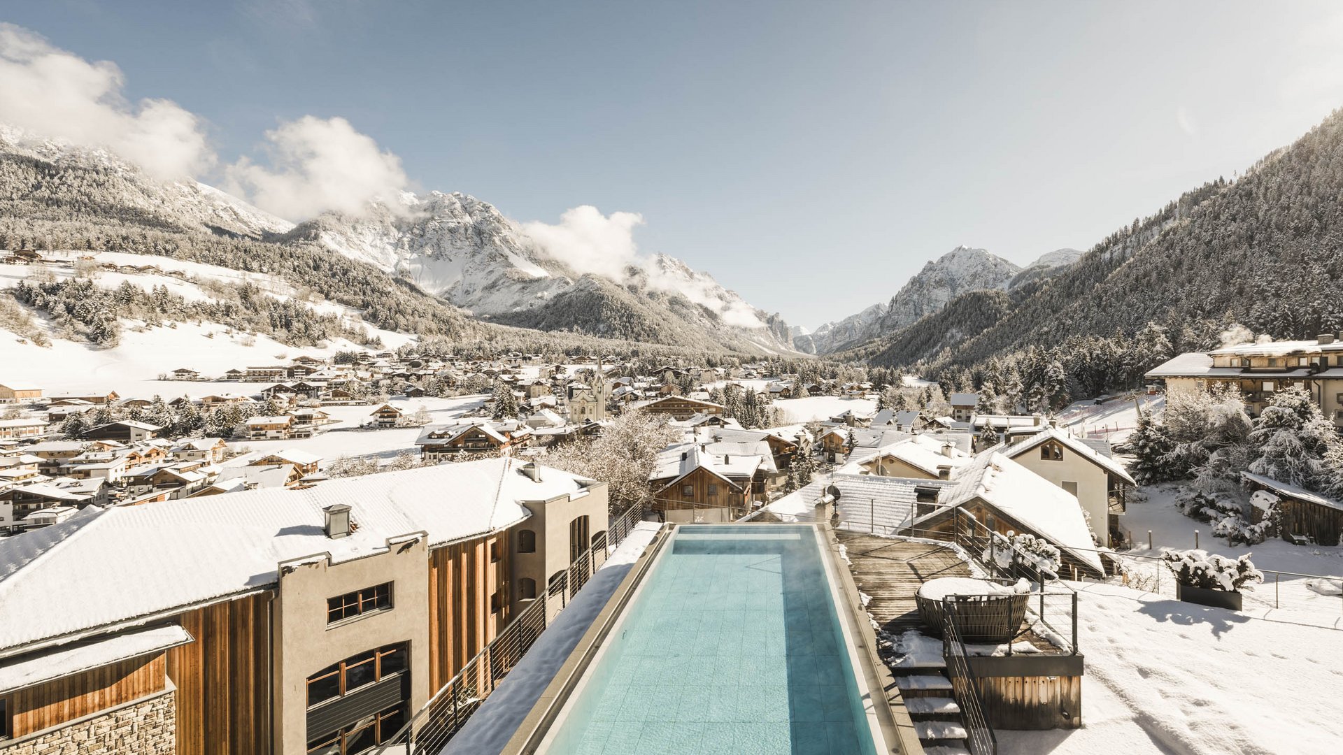 Wellnesshotel in Südtirol: Auf in den Traumurlaub! Beheizter Pool auf Dach mit Blick auf schneebedeckte Alpen und Dorf