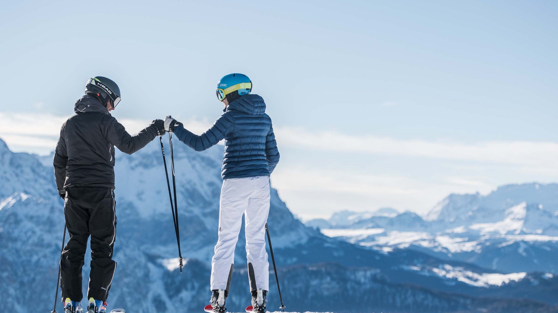 Angebote: Wellness und Wandern | Südtirol Zwei Skifahrer geben sich einen Handschlag vor verschneiten Bergen