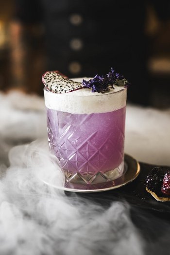 Wellnesshotel in Südtirol: Auf in den Traumurlaub! Lila Cocktail mit Schaum und Früchten auf einem Tablett mit Nebel