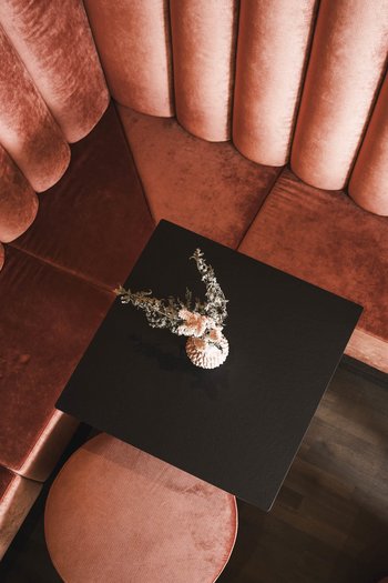 Wellnesshotel in Südtirol: Auf in den Traumurlaub! Rote Samt-Eckbank mit schwarzem Tisch und Blumendekoration von oben