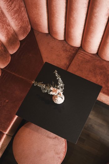 Wellnesshotel in Südtirol: Auf in den Traumurlaub! Rote Samt-Eckbank mit schwarzem Tisch und Blumendekoration von oben