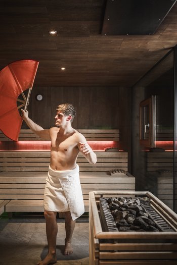 Weekly programme of the “Wanderhotels Südtirol” Man with white towel holding large red fan in sauna room