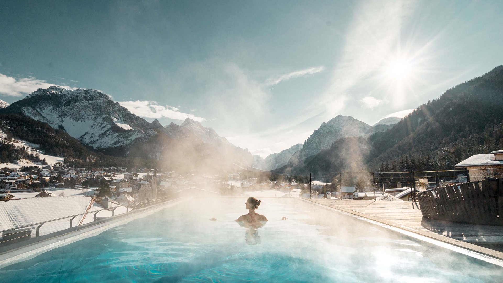 Angebote: Wellness und Wandern | Südtirol Person im beheizten Außenpool mit Blick auf verschneite Berge und sonnigen Himmel