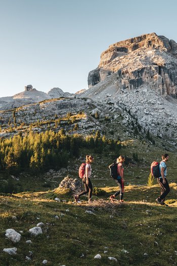 Wellnesshotel in Südtirol: Auf in den Traumurlaub! Drei Wanderer mit Rucksäcken in bergiger Landschaft bei Sonnenschein