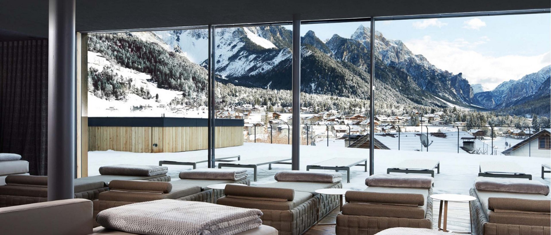 Wellnesshotel in Südtirol: Auf in den Traumurlaub! Lounge mit Aussicht auf verschneite Berge und Dorf durch große Fenster