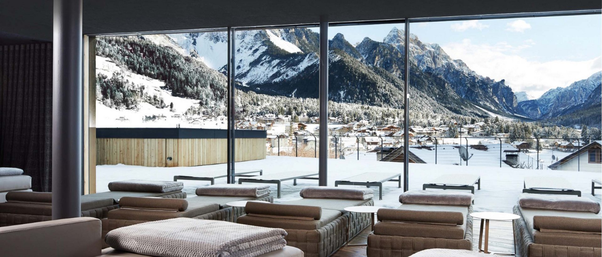 Wellnesshotel in Südtirol: Auf in den Traumurlaub! Lounge mit Aussicht auf verschneite Berge und Dorf durch große Fenster