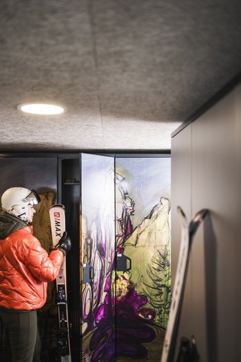 Il nostro hotel sulle piste a San Vigilio di Marebbe Persona con sci e casco davanti a un armadietto colorato in locale sci