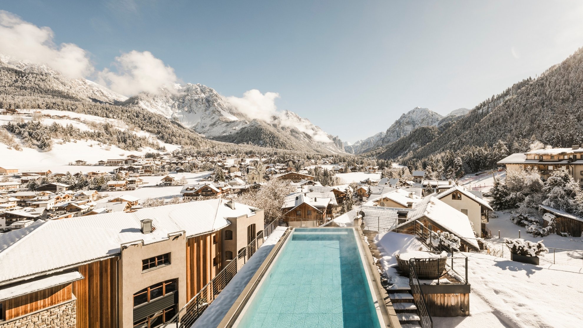Wellnesshotel in Südtirol: Auf in den Traumurlaub! Langer Außenpool vor einem verschneiten Bergdorf und schneebedeckten Alpen