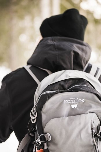 Wellnesshotel in Südtirol: Auf in den Traumurlaub! Wanderer mit grauem Rucksack auf einem verschneiten Waldweg