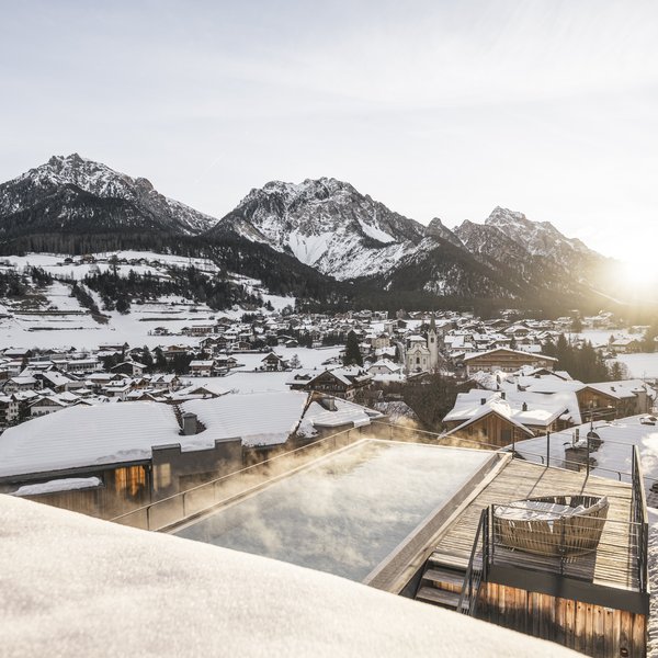 Wellnesshotel in Südtirol: Auf in den Traumurlaub! Sonnenaufgang über verschneitem Bergdorf mit beheiztem Außenpool