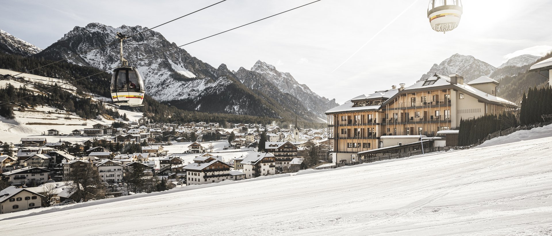 #myexcelsior Sunday News 16.03.2025 Seilbahnkabinen über einem verschneiten Skiort mit Bergen im Hintergrund