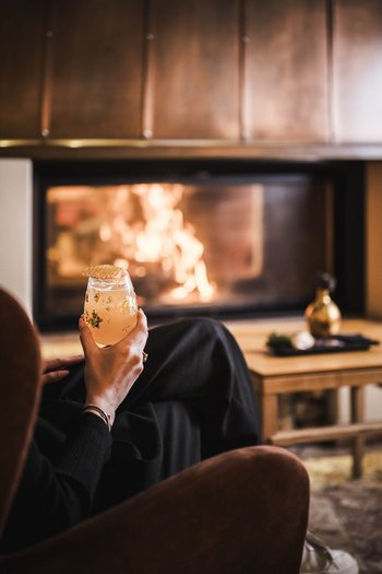 Wellnesshotel in Südtirol: Auf in den Traumurlaub! Person hält ein Getränk vor einem lodernden Kamin