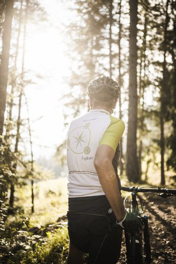 Weekly programme of the “Wanderhotels Südtirol” Man with bike standing in forest looking towards the bright sun