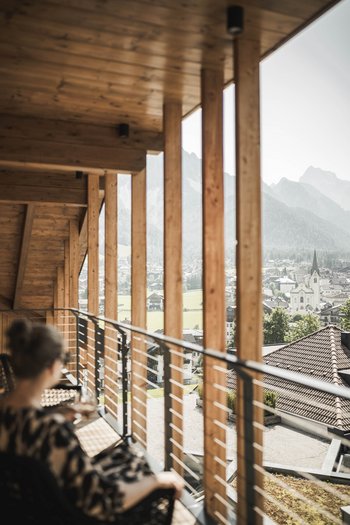 Wellnesshotel in Südtirol: Auf in den Traumurlaub! Person entspannt auf Balkon mit Blick auf Bergdorf und Kirche