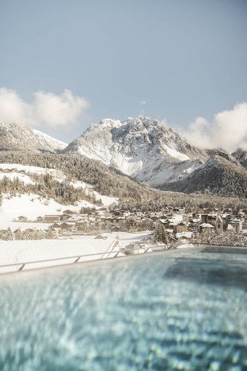 Wellnesshotel in Südtirol: Auf in den Traumurlaub! Verschneites Bergdorf mit Blick auf einen Pool im Vordergrund