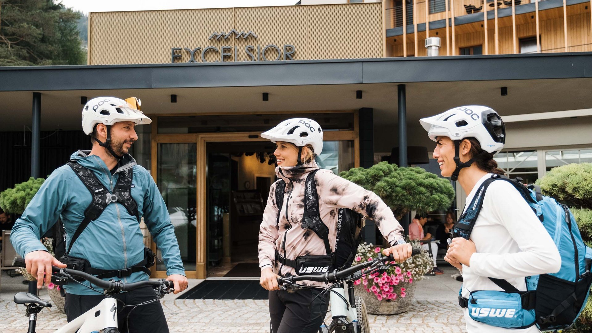 Bike-Leistungen Drei Radfahrer mit Helmen vor dem Hotel Excelsior im Gespräch