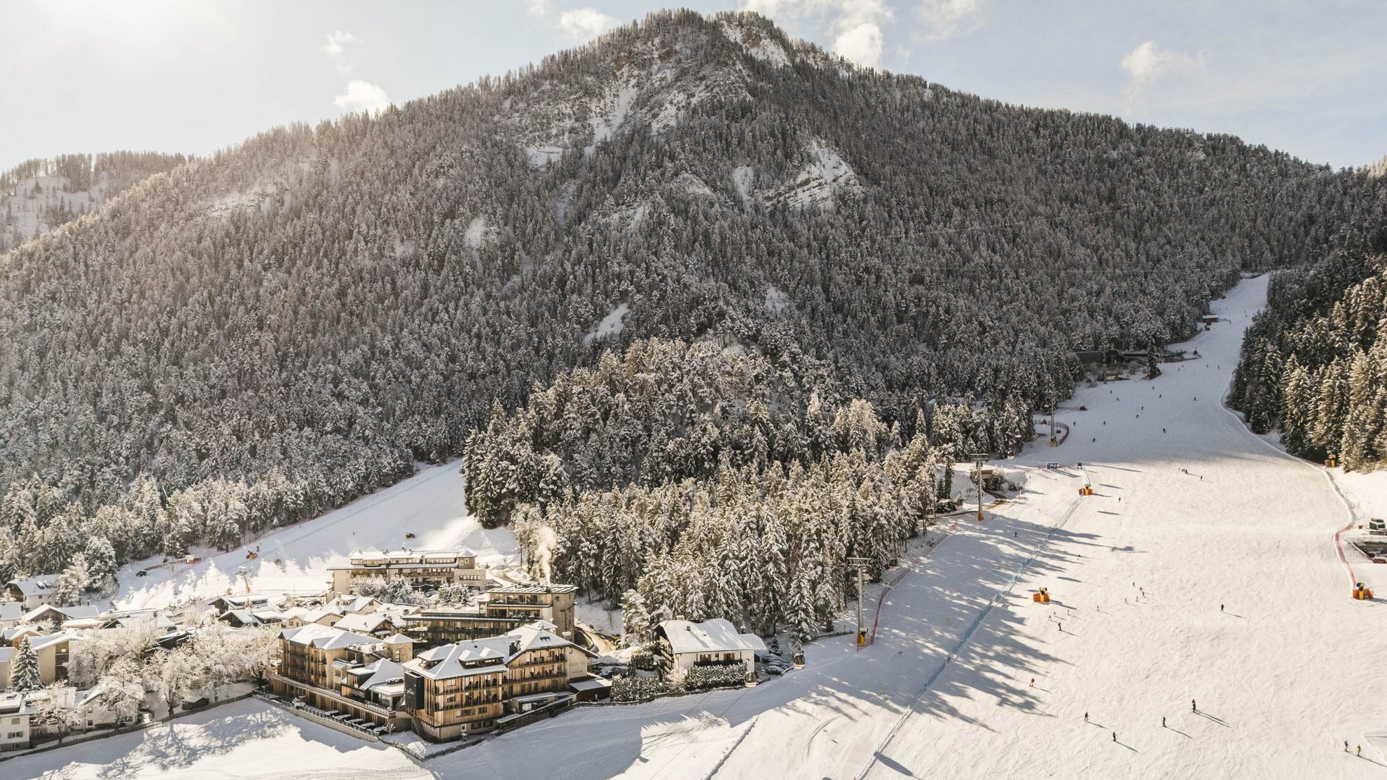 Wellnesshotel in Südtirol: Auf in den Traumurlaub! Verschneites Skigebiet mit Pisten, Liften und Berghotels vor einem bewaldeten Berg