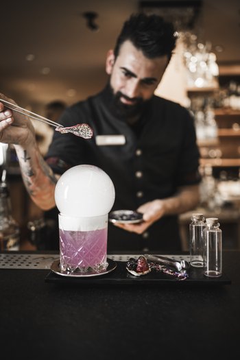 Weekly programme of the “Wanderhotels Südtirol” Bartender preparing a pink cocktail with smoke and garnish