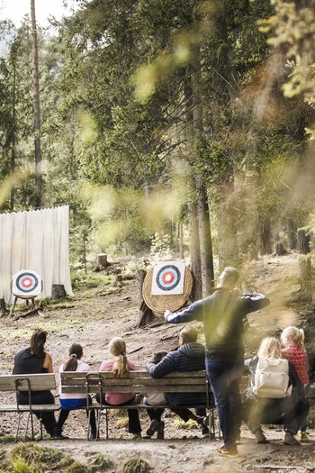 Weekly programme of the “Wanderhotels Südtirol” Children and adults practicing archery in the forest in front of two targets
