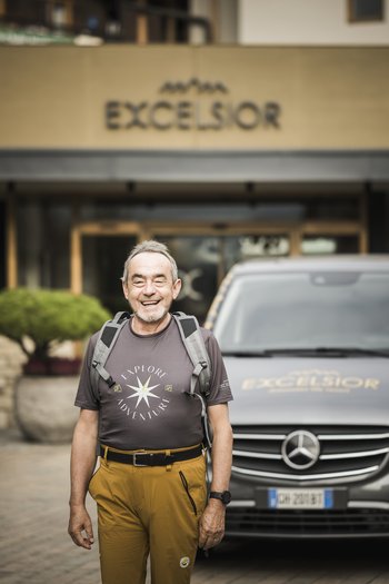 Weekly programme of the “Wanderhotels Südtirol” Smiling man with backpack in front of Excelsior hotel and Mercedes vehicle