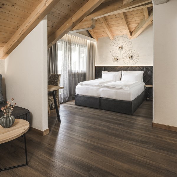 Wellnesshotel in Südtirol: Auf in den Traumurlaub! Gemütliches Hotelzimmer mit Holzbalken, Bett und Sitzbereich
