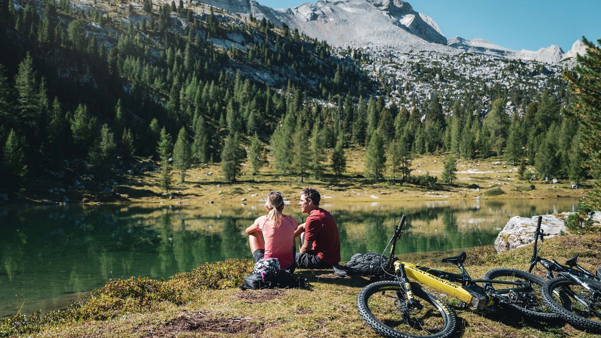 Bike-Leistungen Zwei Radfahrer sitzen am Seeufer in den Bergen mit Mountainbikes neben sich
