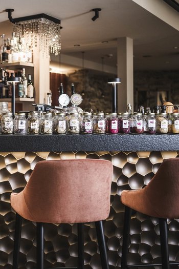 Wellnesshotel in Südtirol: Auf in den Traumurlaub! Bar mit rosa Hockern und vielen Gewürz- und Kräutergläsern auf der Theke